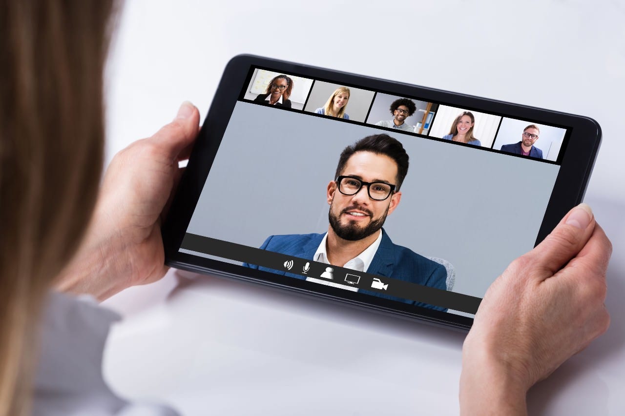 5 professionals converse via video chat on a tablet; hiring across time zones concept