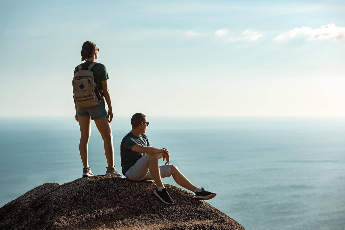 Couple of young hikers are relaxing on big rock against sea and sky