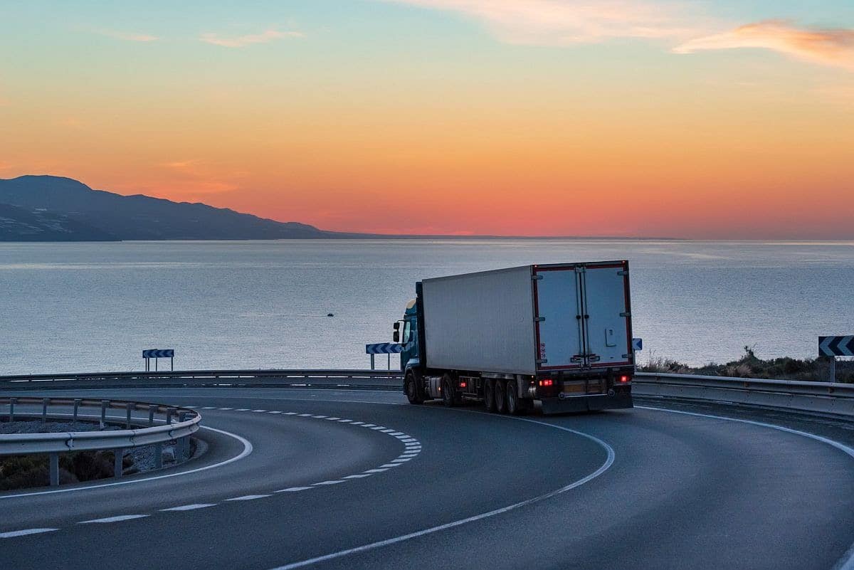 Truck with refrigerated semi-trailer on a mountain road with the sea and the sun on the horizon; Semiconductor reshoring concept
