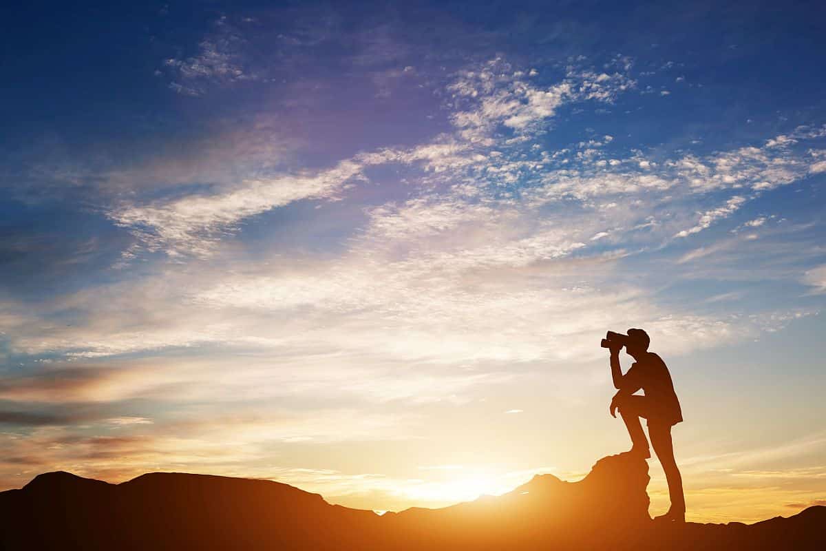Man standing on rocks, looking through binoculars. Looking forward into the future. Sunset scenic sky. 3d illustration.