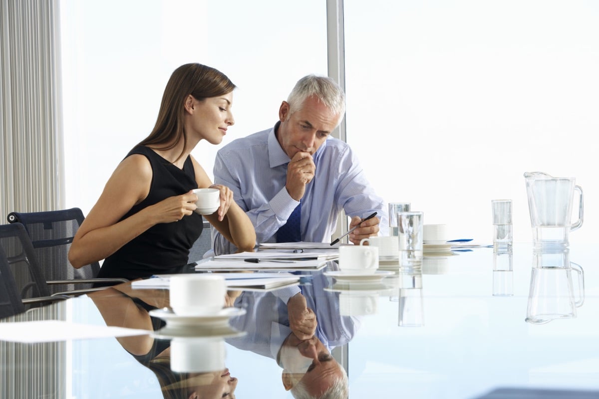 Two Business Colleagues at a Boardroom Table Having Informal Discussions; representing Digital Natives in the workplace
