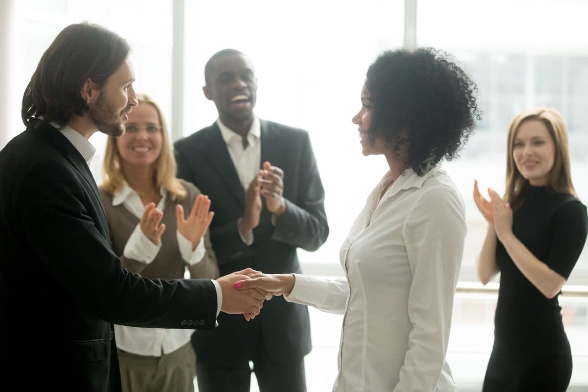 Grateful boss handshaking promoting african businesswoman congratulating with career achievement while colleagues applauding cheering successful worker, appreciation handshake, employee recognition