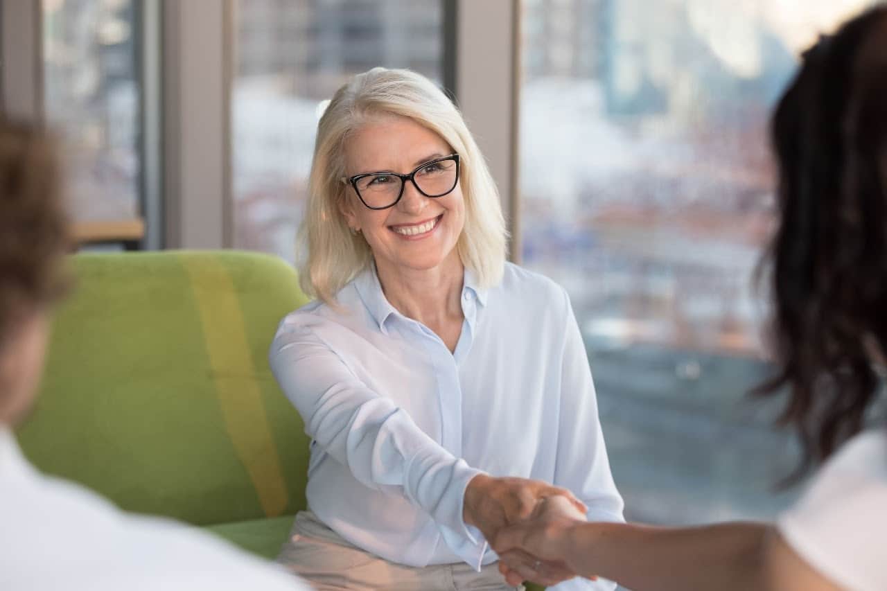 interview at a desk in a modern office, senior leader shakes the hand of a younger worker; concept: better job postings will help hire better talent