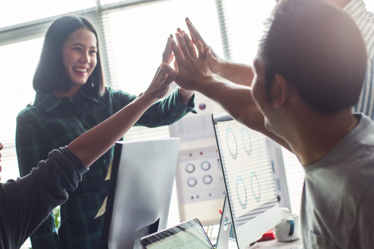 four professionals in an office share a group high-five; HR transformation metrics concept