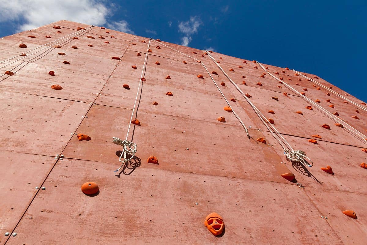 Artificial rock climbing wall with grips for hands and feet in outdoor adventure park; labor shortage concept