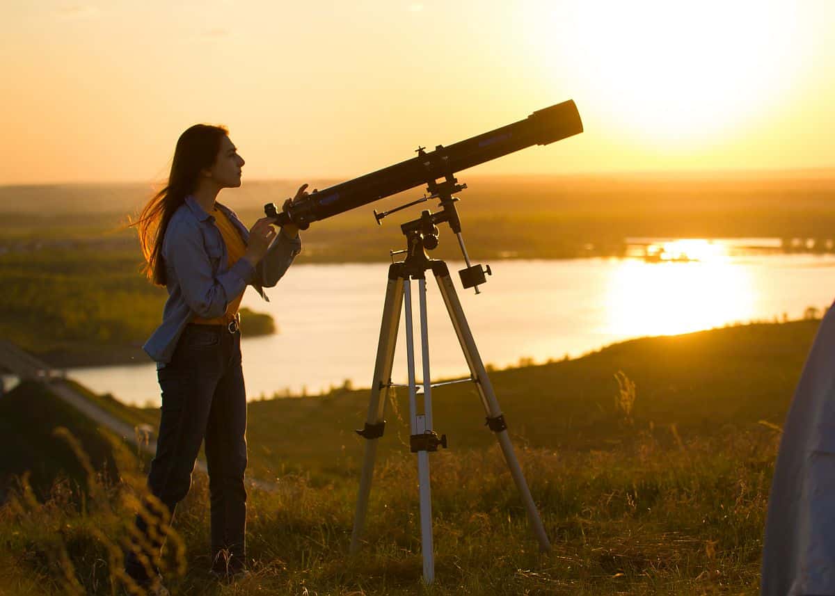 Silhouette of young woman looking through a telescope at sunset; worker-focused hiring concept