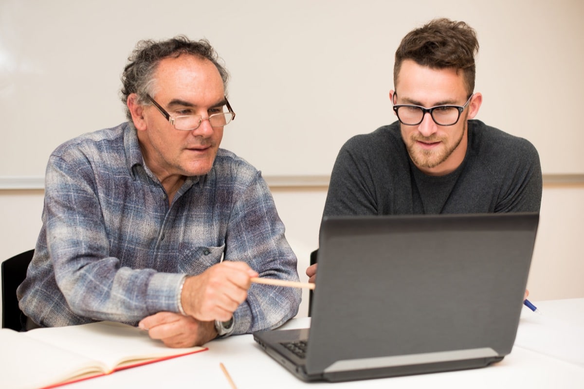 Young man teaching elderly man of usage of computer. Representing older workers staying employed longer.