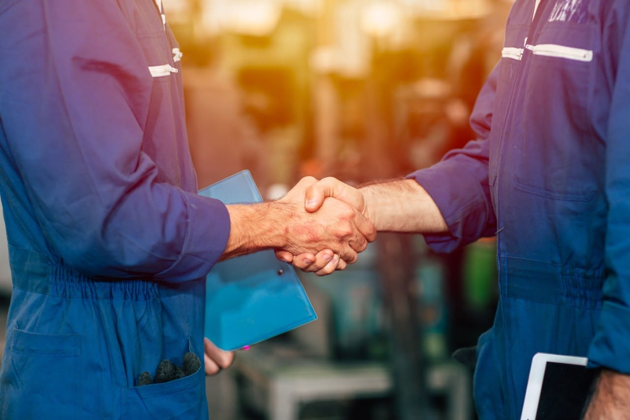 two workers in industrial jumpsuits shake hands; state of talent management in manufacturing concept