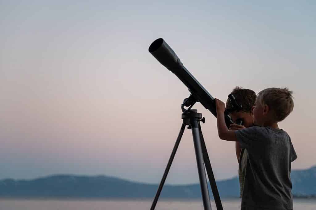 Two brothers, toddler boys, looking at the stars using a telescope by the sea on a beautiful summer night.