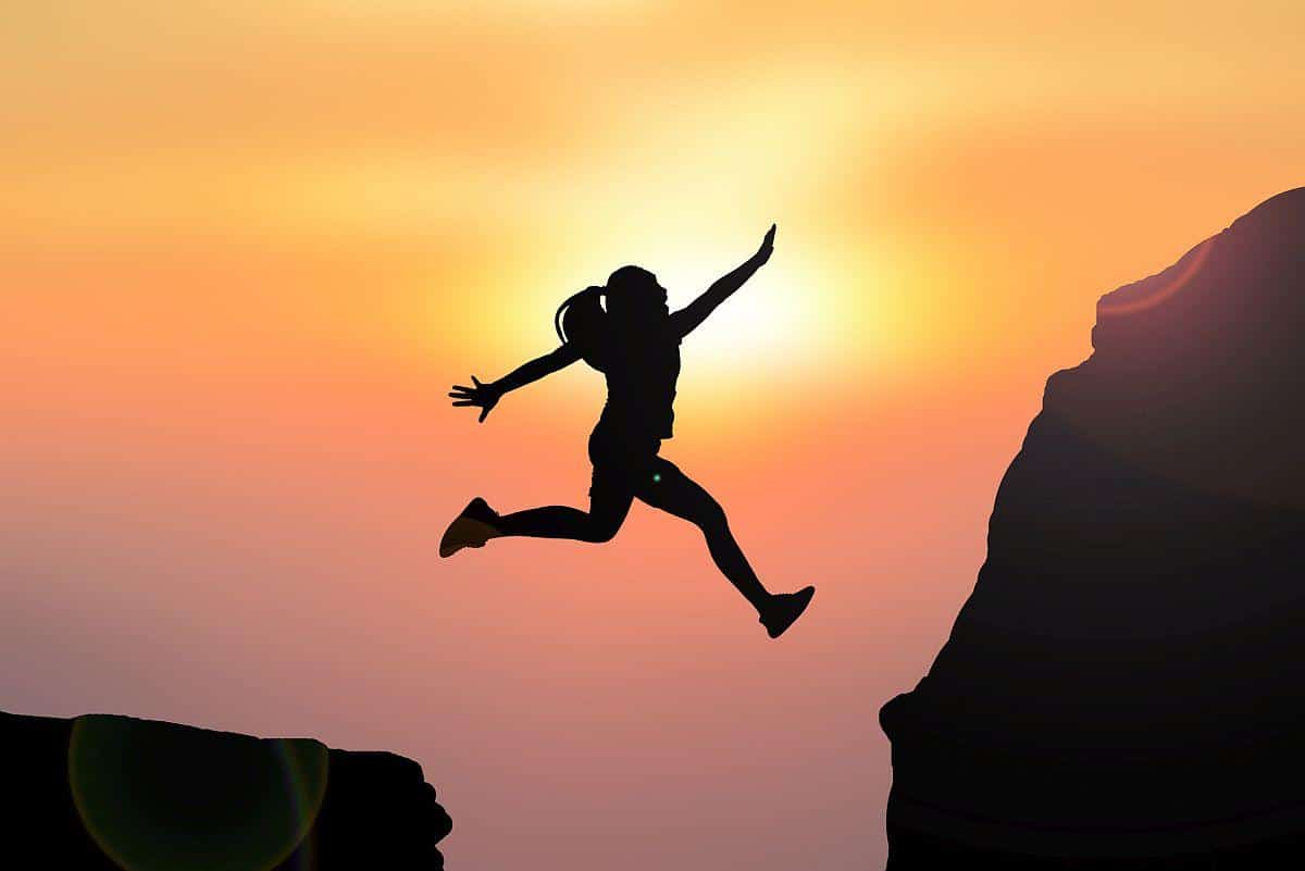 hiker leaps to a ledge with the sunset in the background; succession planning and upskilling concept