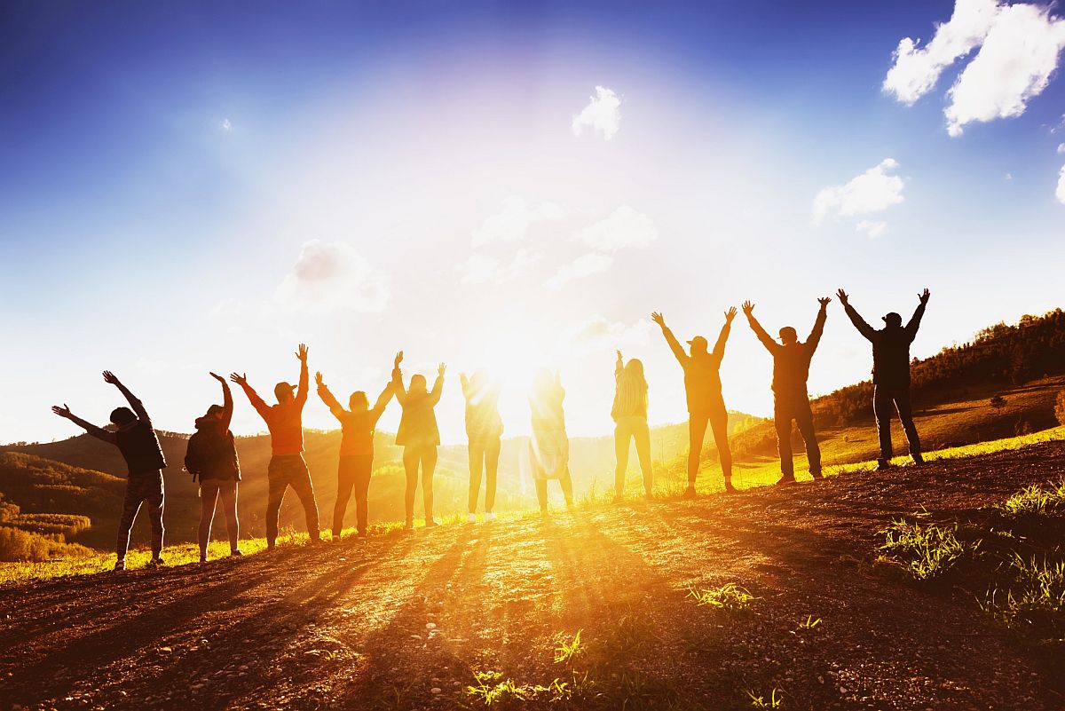 group of people with arms raised backlit by the sunrise; oil and gas industry hiring concept