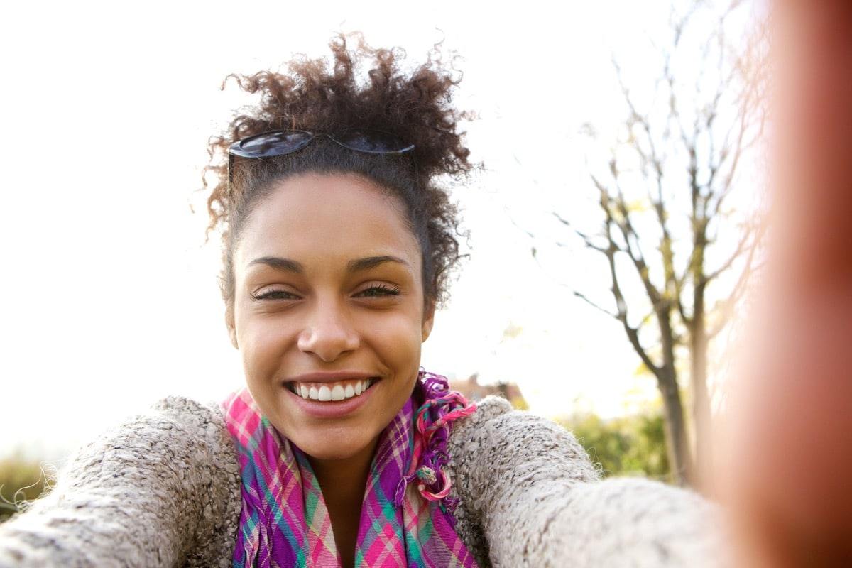 portrait of a young woman smiling and talking a selfie; fostering belonging concept