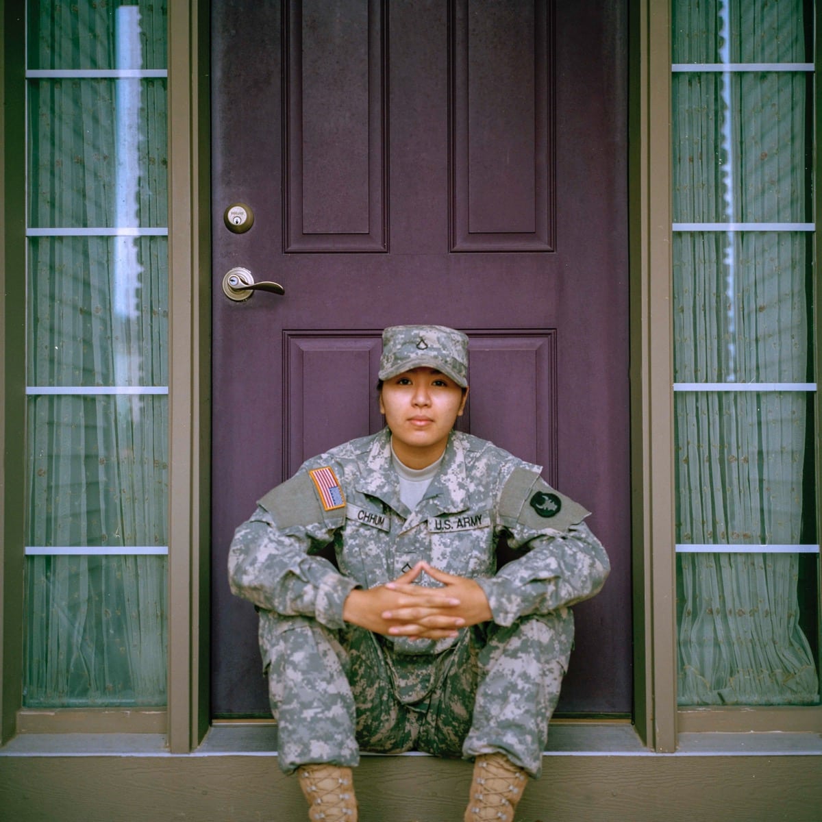 soldier in fatigues sits on stoop of a nice home