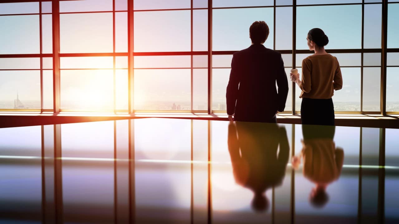 two businesspersons watch the sunset from the window of a modern office; CHRO-CEO partnerships concept