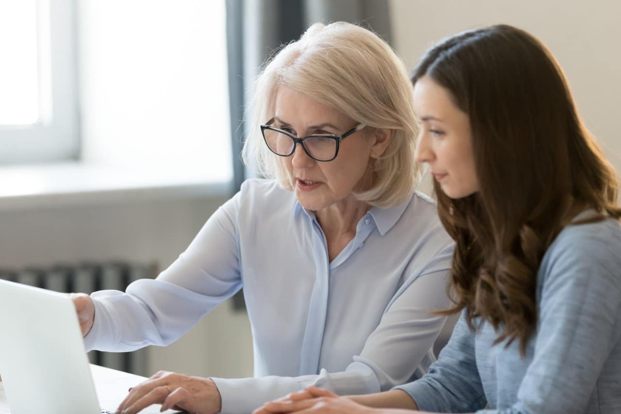 an older worker mentors a young worker at a laptop; succession plan concept